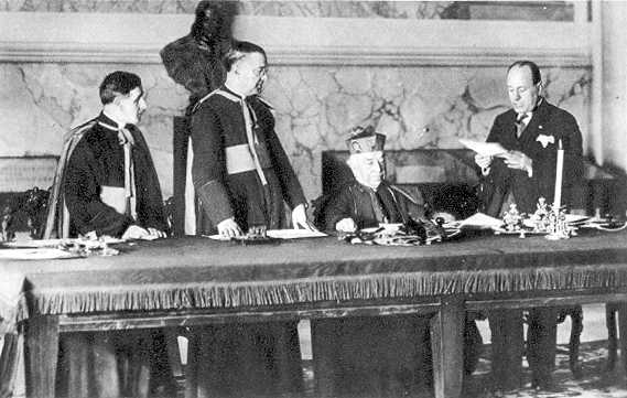 Benito Mussolini reads his credentials prior to signing the Lateran Treaty on behalf of King Victor Emmanuel III. Cardinal Gasparri (seated), signed on behalf of Pope Pius XI.